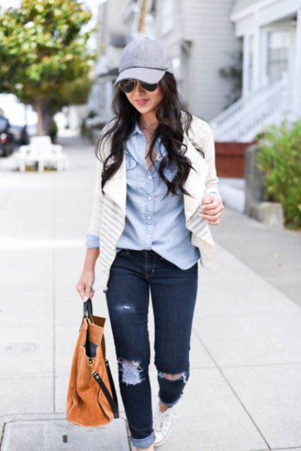 Wearing a light blue shirt, a cardigan with white and gray stripes, cuffed, faded blue jeans, a brown tote bag, and white sneakers.